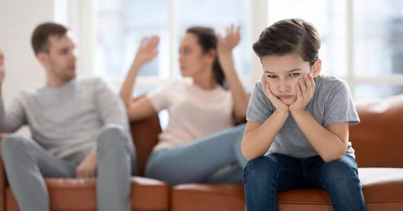 A young boy sits on a couch, resting his hands on his face, displaying a thoughtful or contemplative expression